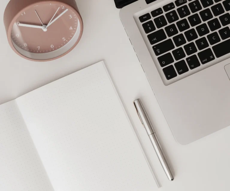 Laptop, Notizbuch und Uhr auf hellem Schreibtisch – Symbolbild für Website-Grundlagen wie Hosting, Domain und WordPress für Gründerinnen.