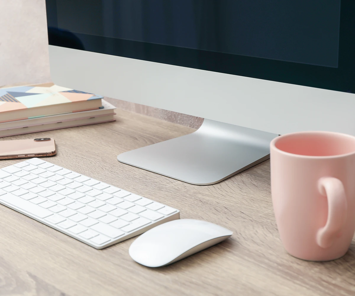 Minimalistischer Arbeitsplatz mit iMac, Tastatur und rosa Tasse – Fokus auf WordPress Website-Pflege und Plugins.